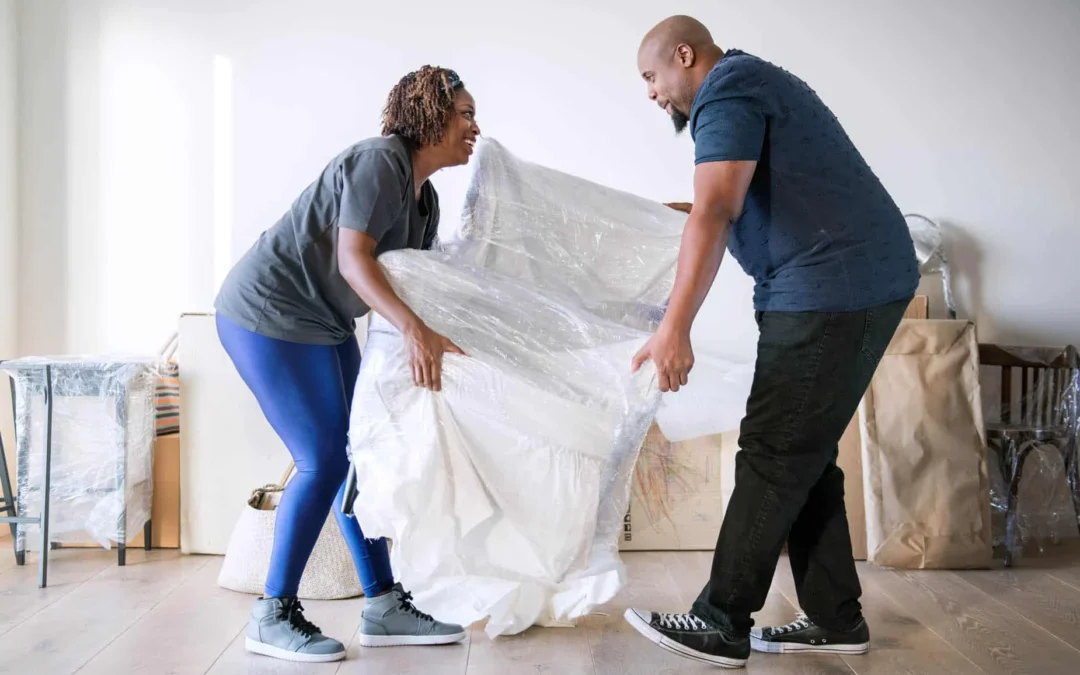 Couple lifting a large wrapped item together during a home move in a bright room
