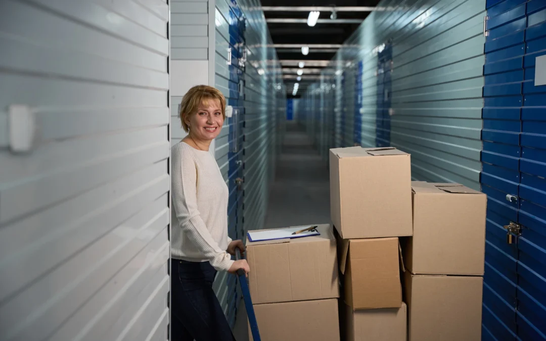 Smiling woman pushing a hand truck loaded with boxes down a storage facility hallway.
