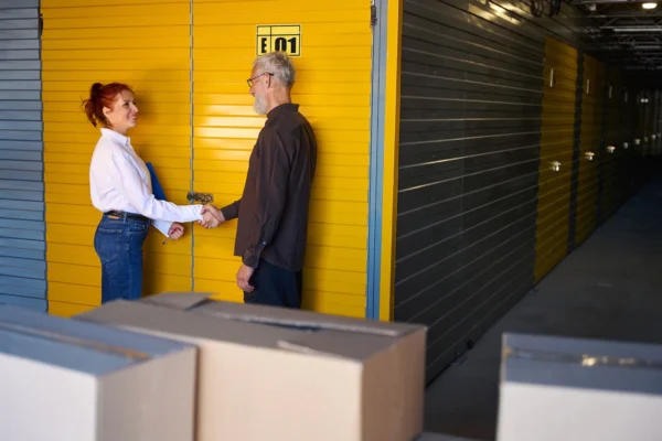 Two people shake hands in a storage facility corridor, standing by bright yellow unit doors while smiling at each other.